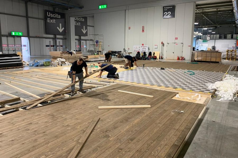 Squadra al lavoro sulla pavimentazione in legno di un allestimento in un padiglione fieristico
